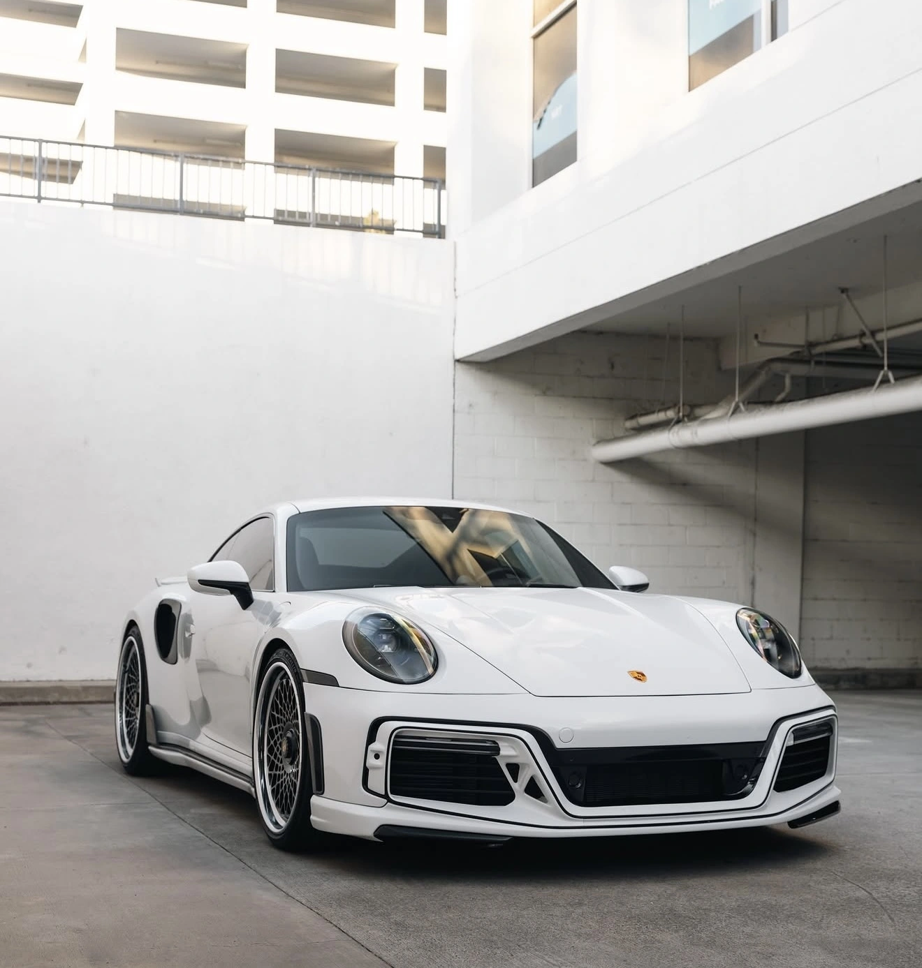 White Porsche front-three-quarter view in a concrete garage, editorial